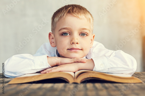 Smiling boy. Cheerful little clever boy sitting at the table with his hands on the book