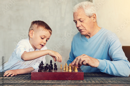 Playing chess. Attentive smart serious men of different generations playing chess while sitting at the table