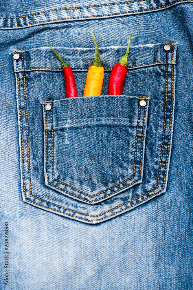 Pocket of jeans staffed with red and yellow chilly peppers, denim  background. Peppers in back pocket of blue jeans. Piquant secret in pocket  of pants, top view. Hot sensations concept Stock Photo