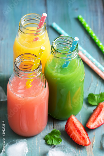 Colorful drinks in bottles . Pink, yellow and green drink on a blue wooden table