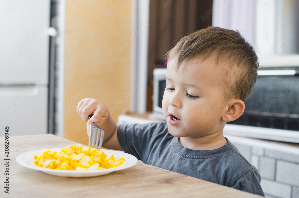 a child in a t-shirt in the kitchen eating an omelet, a fork