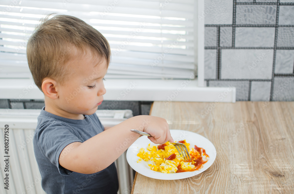 a child in a t-shirt in the kitchen eating an omelet, a fork