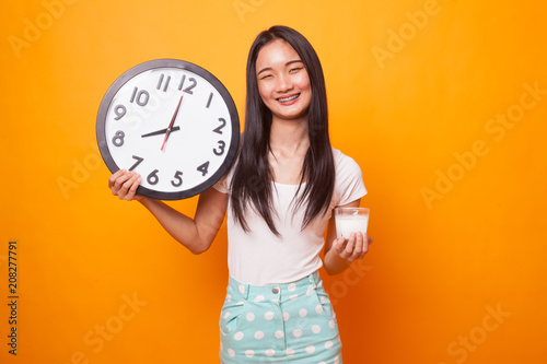Healthy Asian woman drinking glass of milk hold clock.