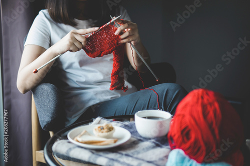 Close up shot of young woman hands knitting a red scarf handicraft in the living room on terrace at home