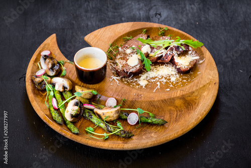 Grilled meat with vegetables in wooden plate on black background