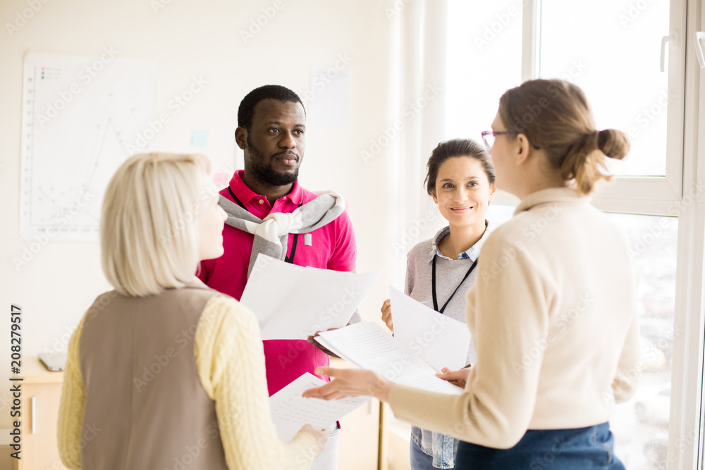 Three young women and black man holding papers in hands and standing in light conference hall Three young women and black man holding papers in hands and standing in light conference hall