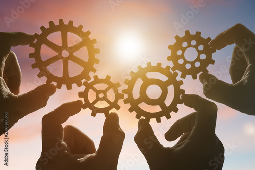 four hands collect a puzzle of gears, against the background of the sky at sunset. Business concept idea. Strategy cooperation, teamwork, creativity, innovation.