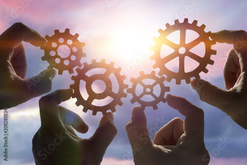 four hands collect a puzzle of gears, against the background of the sky at sunset. Business concept idea. Strategy cooperation, teamwork, creativity, innovation.