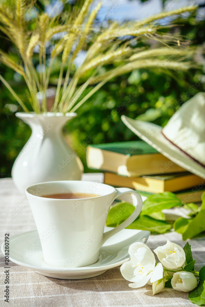A cup with tea, a laptop, a computer, a bookshine table in the garden on a summer morning, a place to work, a concept of freelancing A cup with tea, a laptop, a computer, a bookshine table in the garden on a summer morning, a place to work, a concept of freelancing