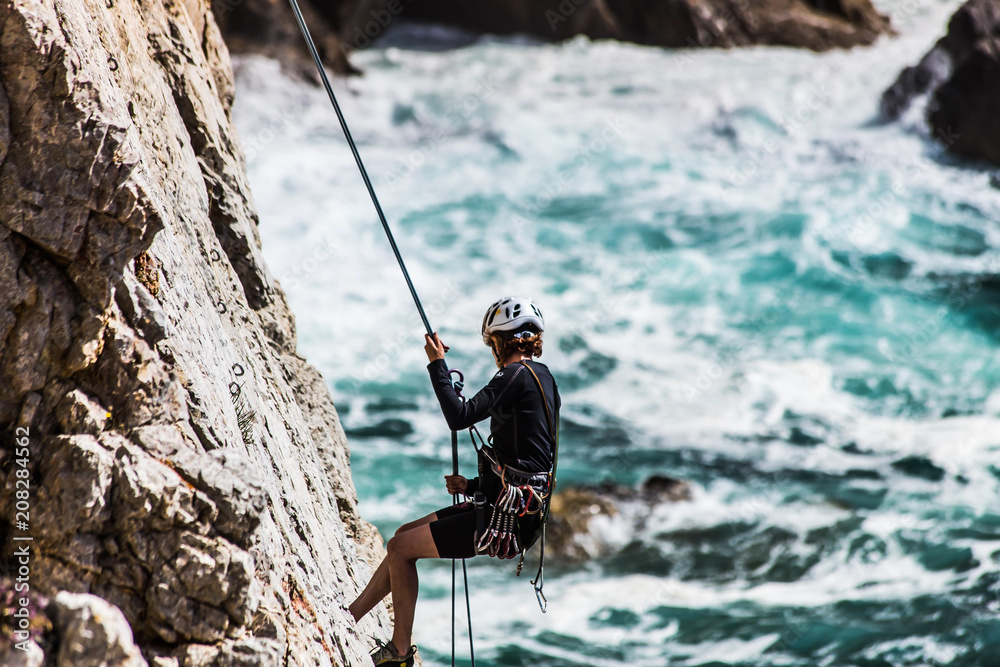 Frau mit Helm klettert mit Seil an steiler Wand , darunter das brausende  meer Stock Photo | Adobe Stock