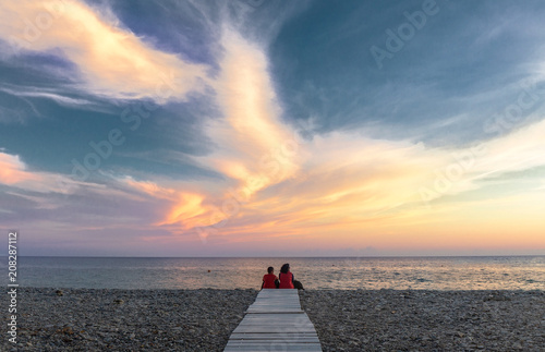 Mom and son sit on the beach and enjoy the sunset