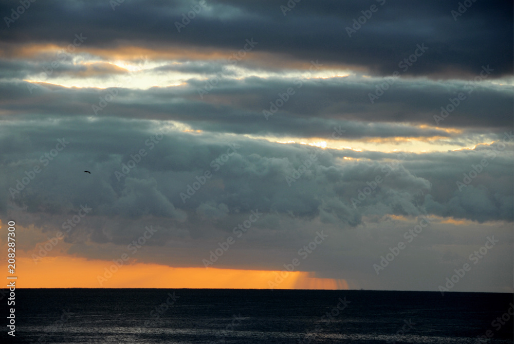 sunset with sun behind dark gray clouds with sliver of orange sky below on horizon