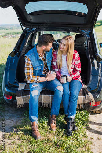 couple of stylish tourists with coffee cups sitting on car trunk in rural field © LIGHTFIELD STUDIOS