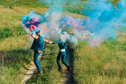 back view of couple holding colorful smoke bombs in rural field