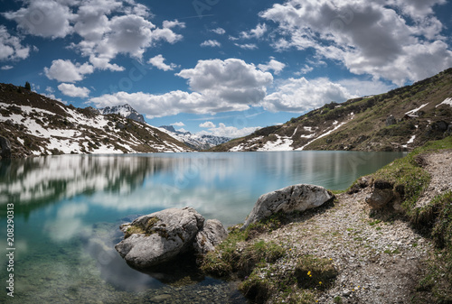 gorgeous mountain lake in the Alps with reflections and snow remnants photo