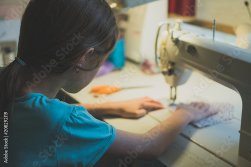 Little girl working on sewing machine at home. Close-up view.