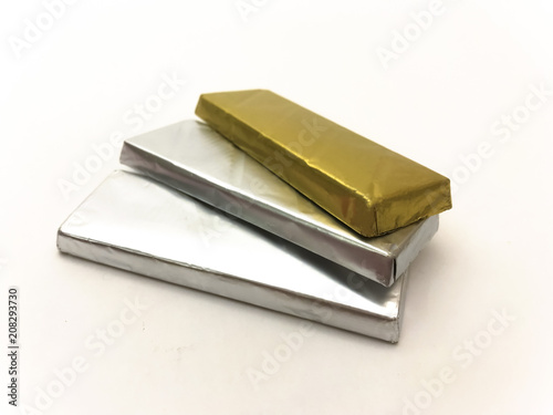 Three chocolate bars in foil on a white background look like gold and silver bars