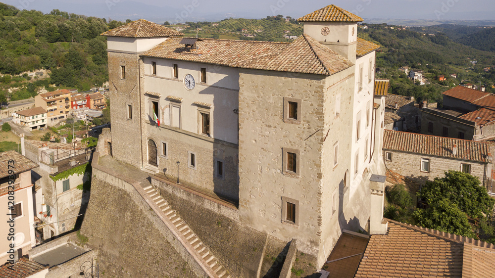Aerial view of Castelnuovo di Porto castle, near Rome in Italy. The building has a square shape with four towers at the corners. On the facade there is a clock and around the houses of the village.