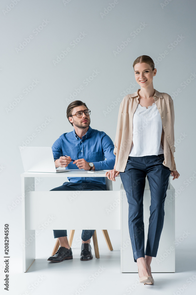 young businessman sitting at workplace while his colleague sitting on his desk on white