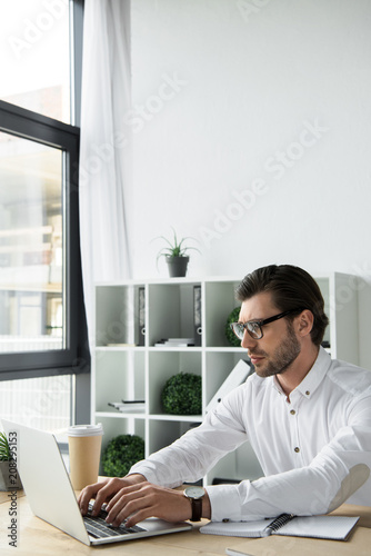 focused young businessman working with laptop at modern office