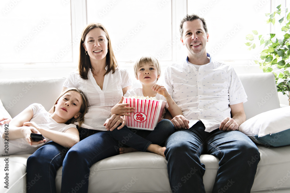 Family of four having fun on the sofa at home watching movie with popcorn Family of four having fun on the sofa at home watching movie with popcorn