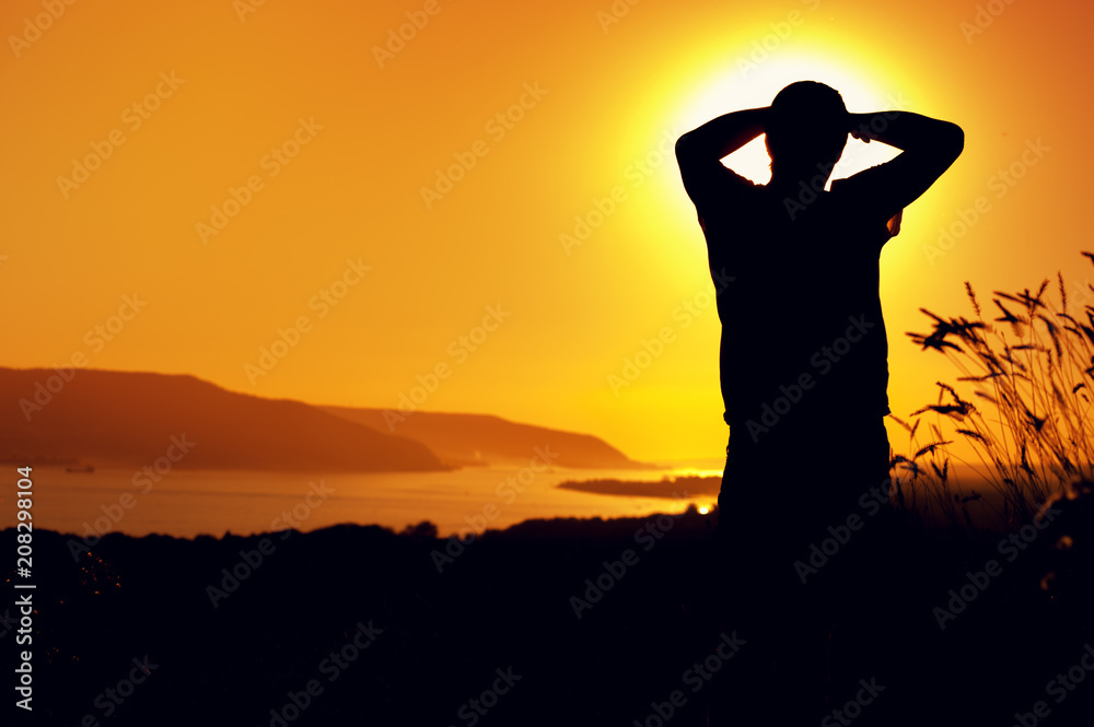 Silhouette of relaxed man enjoying sunset time, watching at river or lake water. Relaxation and leisure concept. Copyspace