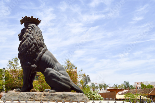 A large beautiful stone statue of a black proud majestic lion on a pedestal against a blue sky and copy the place. photo