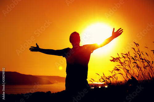 Silhouette of relaxed man enjoying sunset time, raising hands to the sky. Travelling and vacation concept.