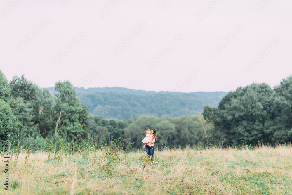 Mother and little daughter playing together in a park. Happy cheerful family. Mother and baby kissing, laughing and hugging in nature outdoors Mother and little daughter playing together in a park. Happy cheerful family. Mother and baby kissing, laughing and hugging in nature outdoors