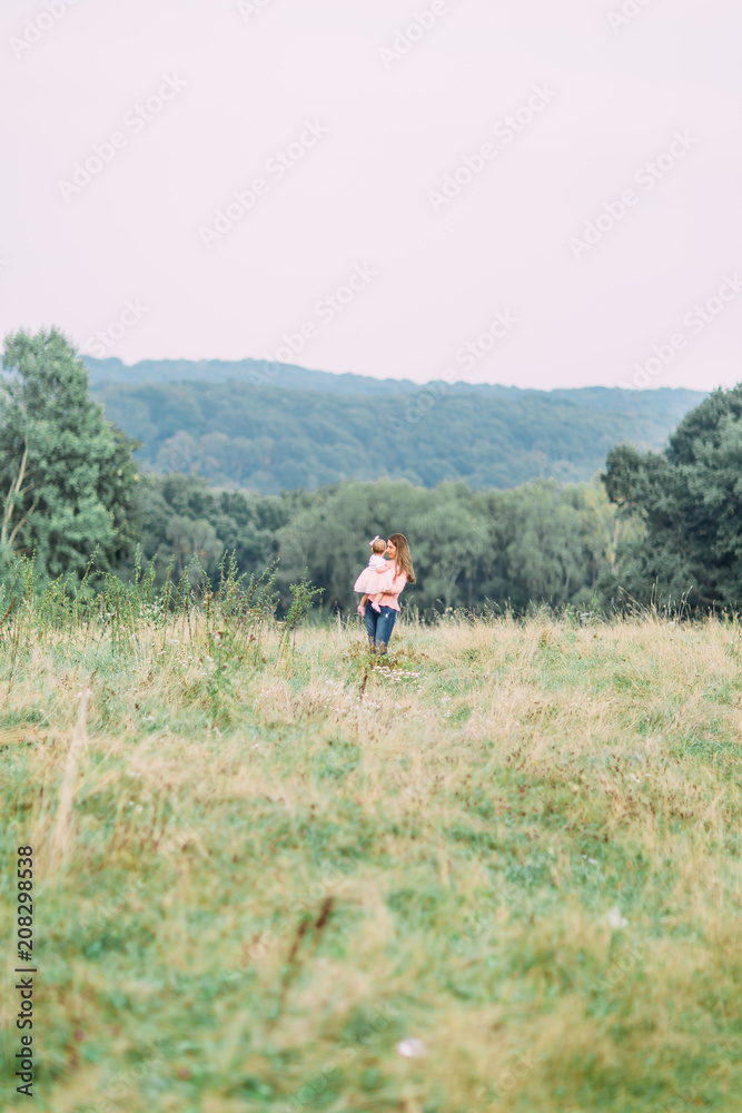 Mother and little daughter playing together in a park. Happy cheerful family. Mother and baby kissing, laughing and hugging in nature outdoors