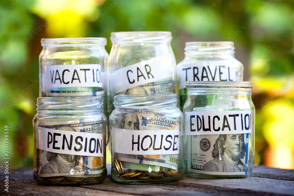 Glass jars with dollars and text: house,car, travel, education,pension,vacation Glass jars with dollars and text: house,car, travel, education,pension,vacation