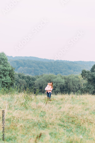 Mother and little daughter playing together in a park. Happy cheerful family. Mother and baby kissing, laughing and hugging in nature outdoors
