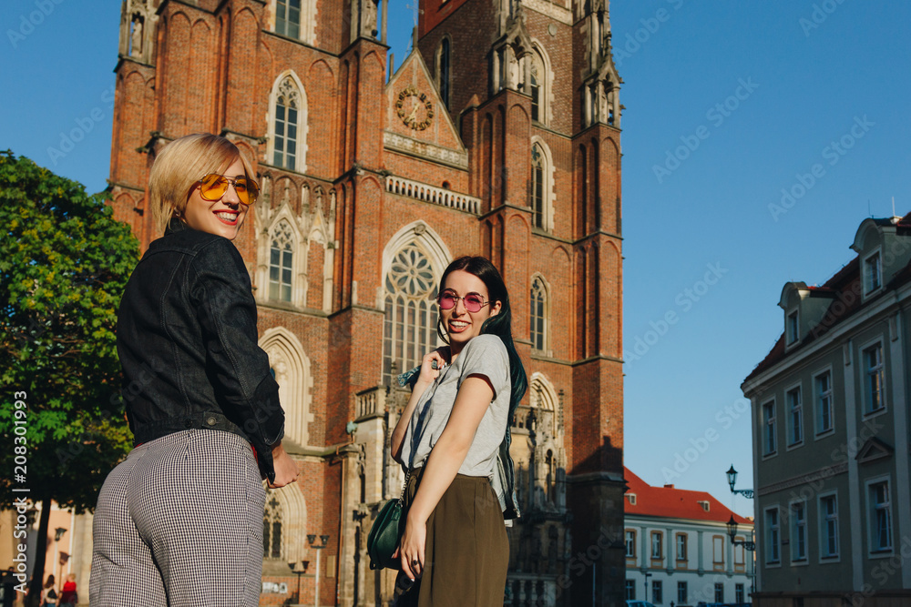 Fototapeta premium two attractive smiling women standing in front of wroclaw cathedral and looking at camera