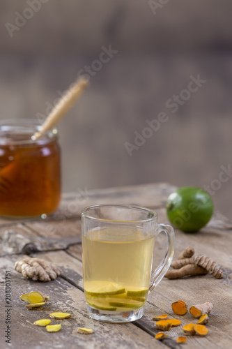 Energy tonic drink with turmeric, ginger, lemon and honey in glass mug, wooden table