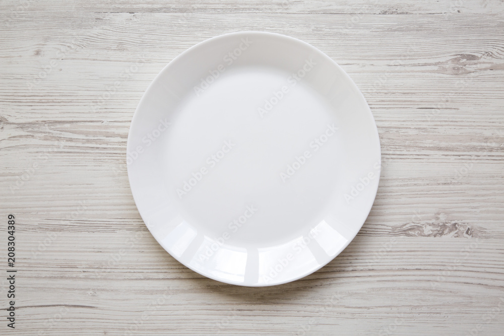 White plate on white wooden background, top view. White plate on white wooden background, top view.
