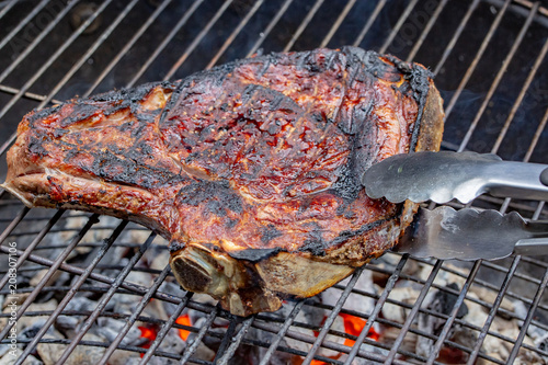 Grilled beef rib on a barbecue grill caught with special pliers photo