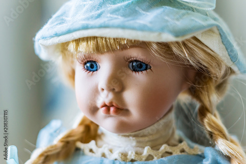 Close-up of beautiful porcelain doll with blond hair and blue eyes, sky blue vintage dress and leather shoes. Little princess games.