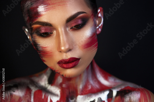 the Euro-Asian woman looks down, the red lips on a black background are well underline the image, a metallic red makeup.