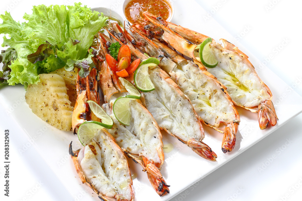 Grilled Cut-off black tiger shrimps with boiled potatoes, slice of limes, fresh vegetables and chili sauce on white square plate, isolated on white background, Close-up macro high angle top view. Grilled Cut-off black tiger shrimps with boiled potatoes, slice of limes, fresh vegetables and chili sauce on white square plate, isolated on white background, Close-up macro high angle top view.