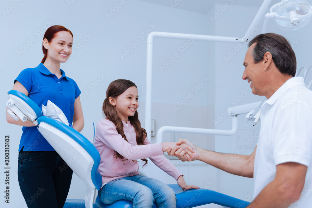 Well done. Charming brunette feeling happiness while shaking hands with doctor and sitting on the chair Well done. Charming brunette feeling happiness while shaking hands with doctor and sitting on the chair