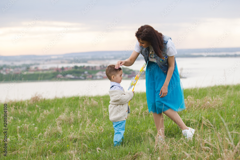 Portrait of a young mother with child walking at summer evening meadow