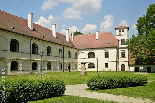White building of former monastery with red roofs and chimneys standing in a green garden, sandy paths, lamps, today a museum in Predklasteri, close to Brno, Czech Republic, Europe