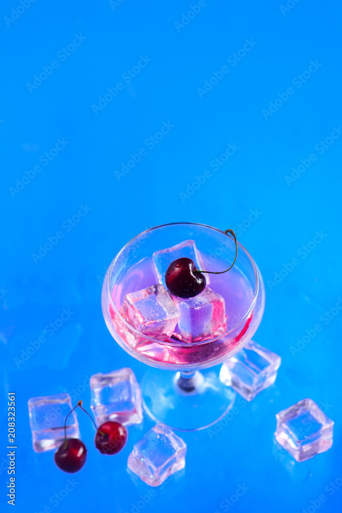 Champagne glass with ice cubes and cherries from above on a blue background. Refreshing cold drink flat lay with copy space