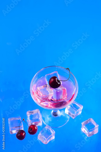 Champagne glass with ice cubes and cherries from above on a blue background. Refreshing cold drink flat lay with copy space