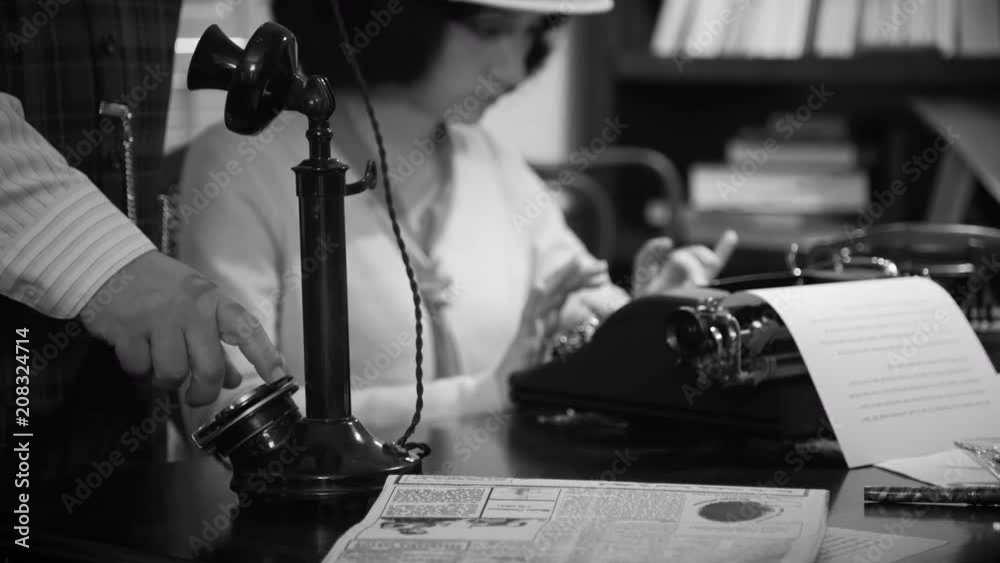 A man dialing a number on a candlestick telephone with female reporter typing in the background.