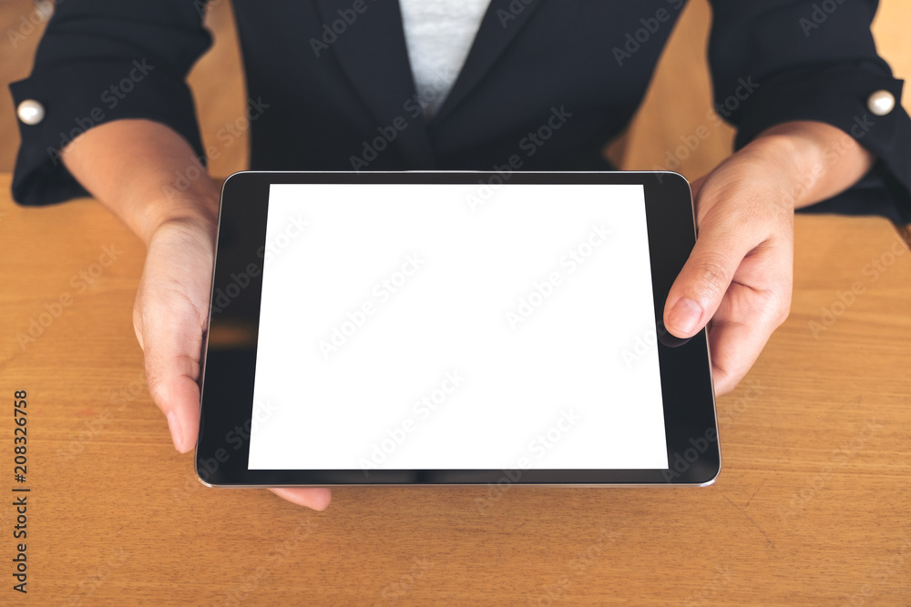 Mockup image of businesswoman holding and showing a black tablet pc with blank white desktop screen on table Mockup image of businesswoman holding and showing a black tablet pc with blank white desktop screen on table