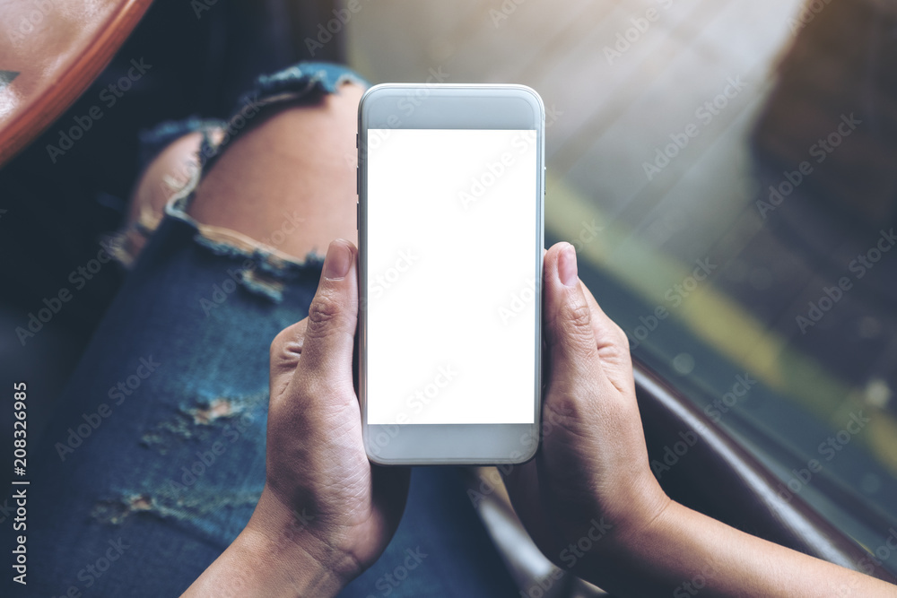 Top view mockup image of woman's hands holding white mobile phone with blank screen
