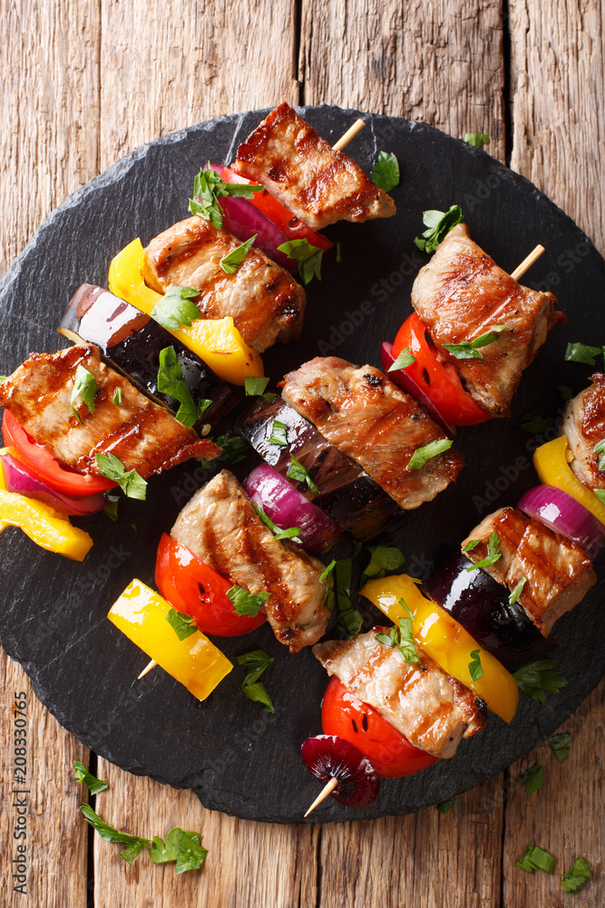 Freshly prepared pork skewers with vegetables close-up on a slate plate. Vertical top view from above Freshly prepared pork skewers with vegetables close-up on a slate plate. Vertical top view from above
