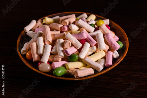 Ceramic dish with the different multi colored candies on a dark wooden table