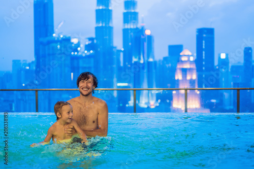 Father and son in outdoor swimming pool with city view in blue sky photo